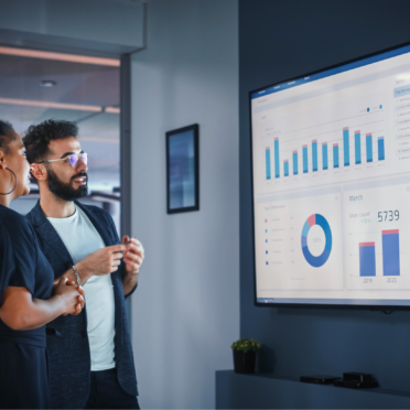 Two marketing professionals reviewing analytics dashboards on a large screen, discussing digital marketing performance data and sales growth strategies.
