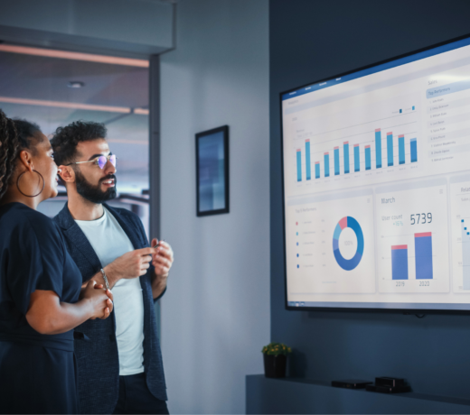 Two marketing professionals reviewing analytics dashboards on a large screen, discussing digital marketing performance data and sales growth strategies.