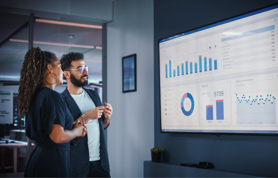 Two marketing professionals reviewing analytics dashboards on a large screen, discussing digital marketing performance data and sales growth strategies.